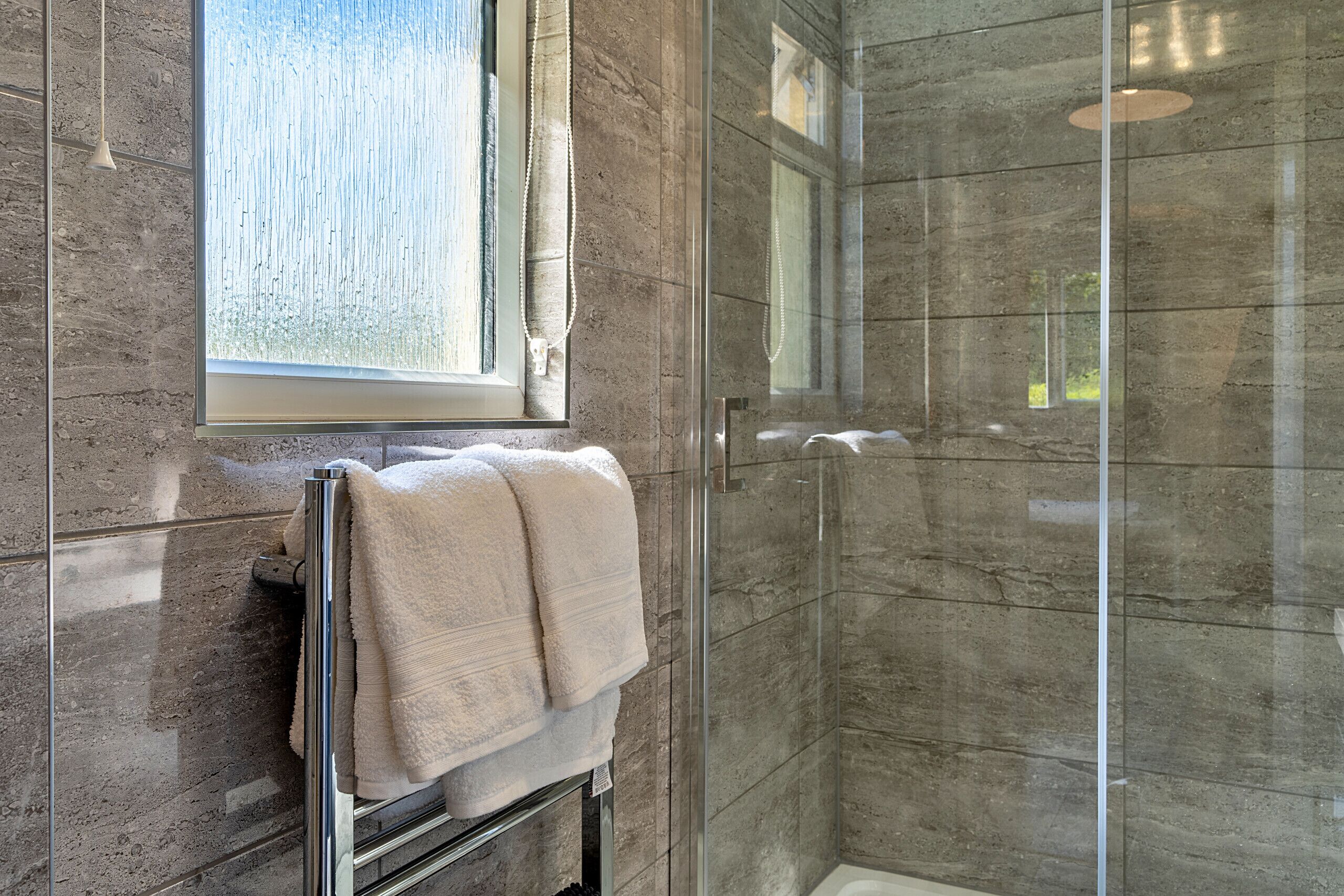 Une salle de bain moderne avec une douche à parois de verre, une fenêtre visible et un porte-serviettes.