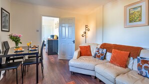 A living room with a sofa, coffee table, and chairs. There is a dining table with plates and glasses. A door leads to another room. - The Annexe at Rosebud Cottage (Wedmore)