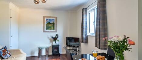 A living room with a sofa, a coffee table with croissants, a TV, and a window with curtains.