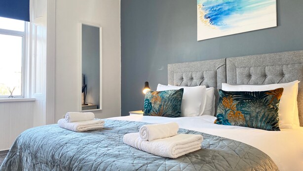 A hotel room with a large bed, a grey headboard, and a painting of a blue sky.