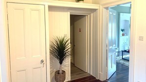 A hallway with a white door, a potted plant, and a wooden floor.