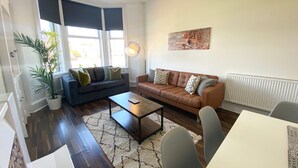A living room with a sofa, coffee table, and chairs. There is a plant, a lamp, and a painting on the wall.