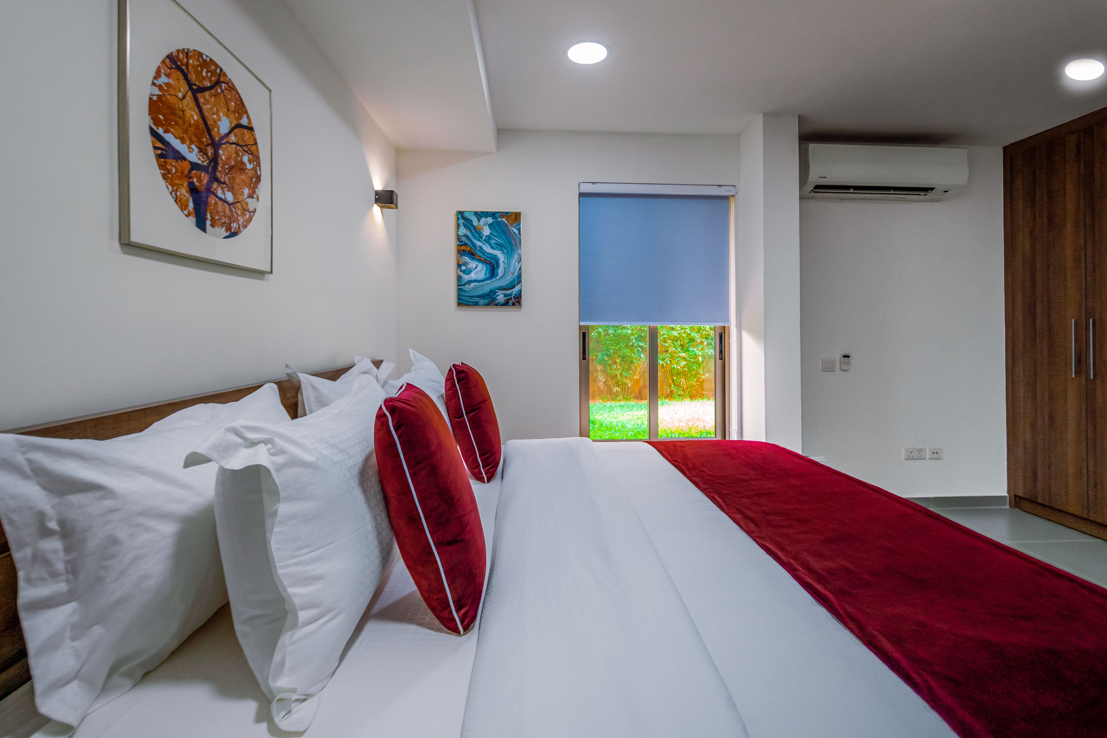 A bedroom with a large bed, white bedding, red pillows, a red throw, and artwork on the walls.