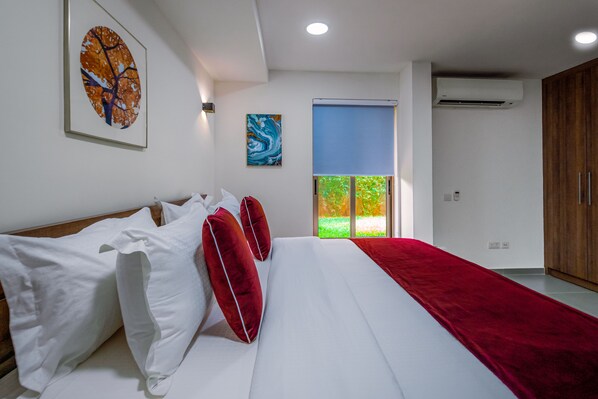 A bedroom with a large bed, white bedding, red pillows, a red throw, and artwork on the walls.