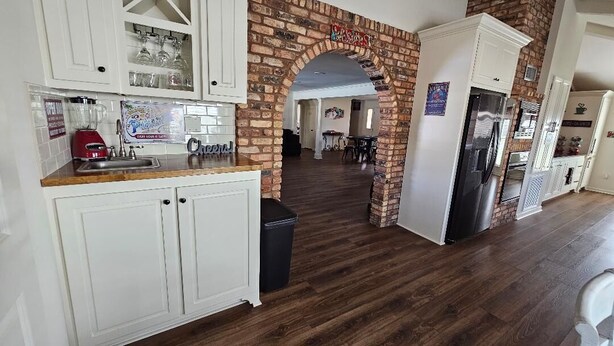A kitchen with white cabinets, a brick archway, and a dining area in the background.