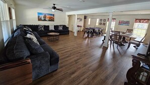 A spacious living room with a dark-colored sofa, a dining area with a table and chairs, and a ceiling fan.