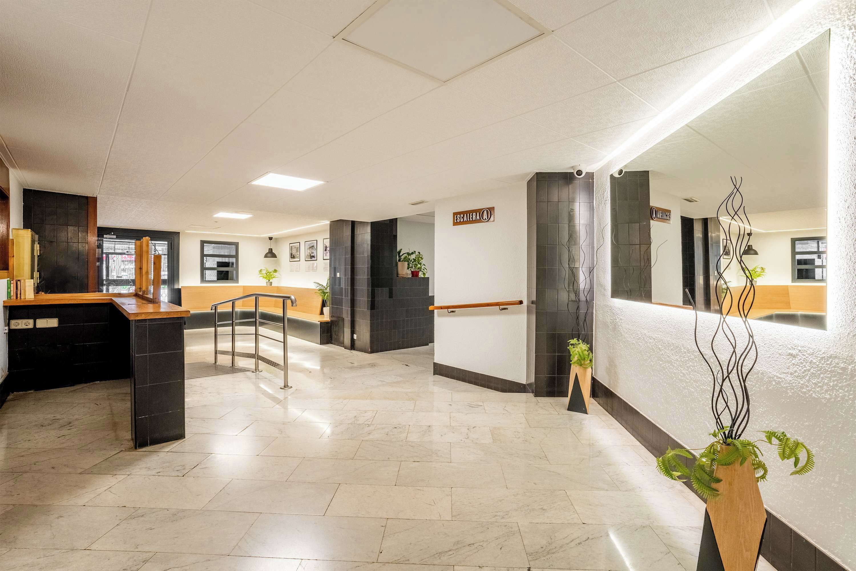 A modern hotel lobby with a reception desk, a staircase, and a reception area.