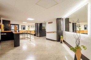 Un hall d’hôtel moderne comprenant un comptoir d’accueil, un escalier et un espace de réception.