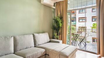 A living room with a sofa, a balcony with a table and chairs, and a view of a building.