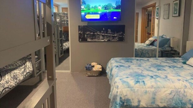 A bedroom with bunk beds, a television mounted on the wall, and a bed with a blue and white patterned bedspread. - Cheerful 4BR/12BD “Ravishing Ranch” (Dayton)