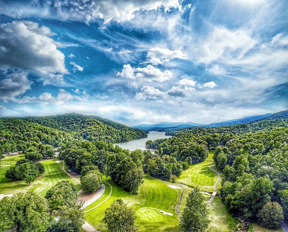 Golfkenttä, jonka taustalla virtaa joki ja kohoaa metsäisiä kukkuloita.