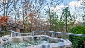 Un bain à remous sur une terrasse extérieure dotée d’une rambarde en métal, entouré d’arbres et avec une structure en bois en arrière-plan.