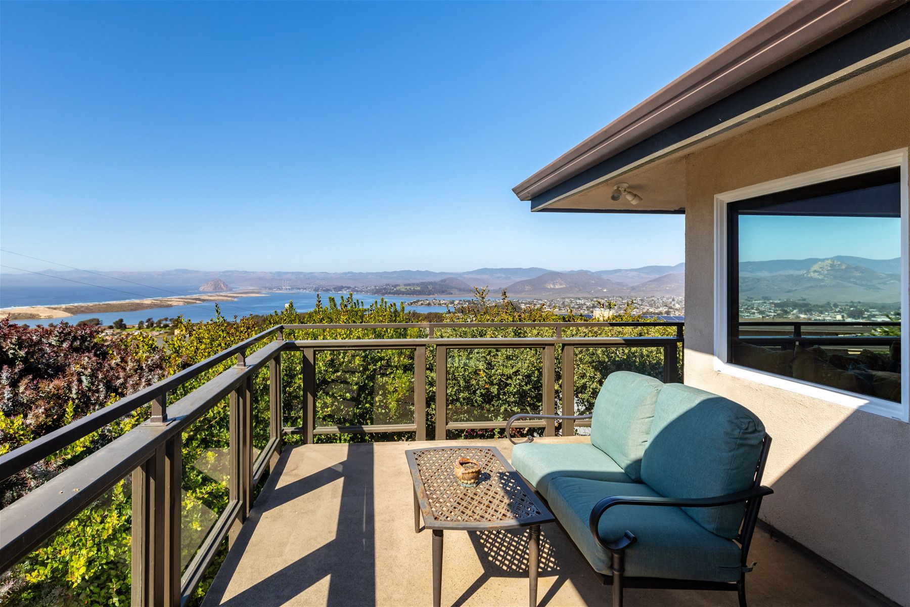 A balcony with a view of the ocean and mountains, a table, and a chair.
