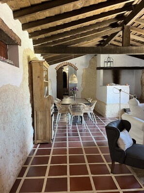 A rustic interior with a tiled floor, a dining area with wicker chairs, a sofa, and a brick fireplace.