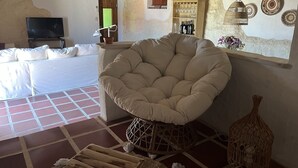 Ett mysigt vardagsrum med en stor sittpuff, en platt-TV, ett träskåp med vinglas och en rustik väggdesign.