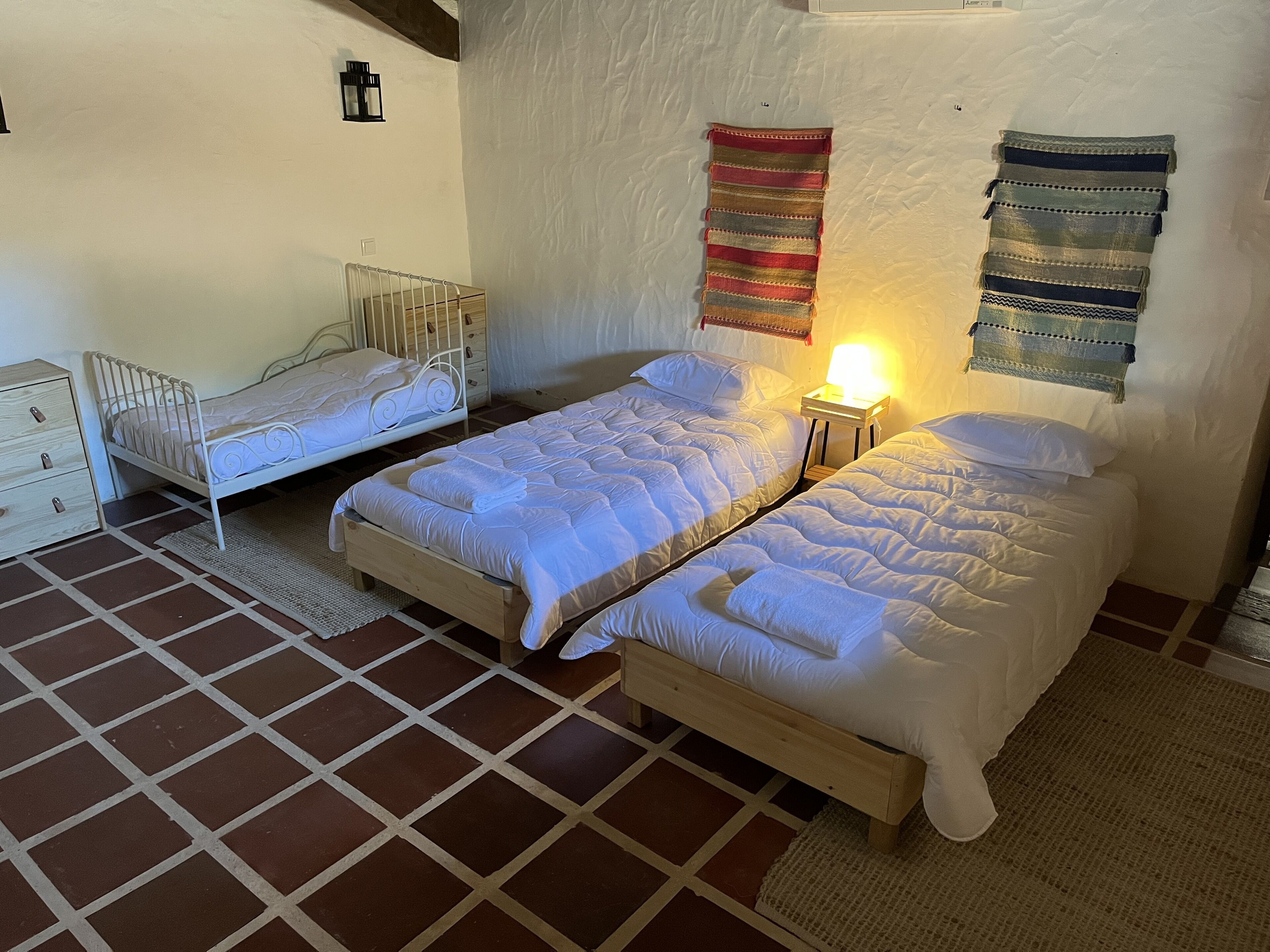 Una habitación con dos camas, una mesita de noche con lámpara, un pequeño aparador y una alfombra estampada.