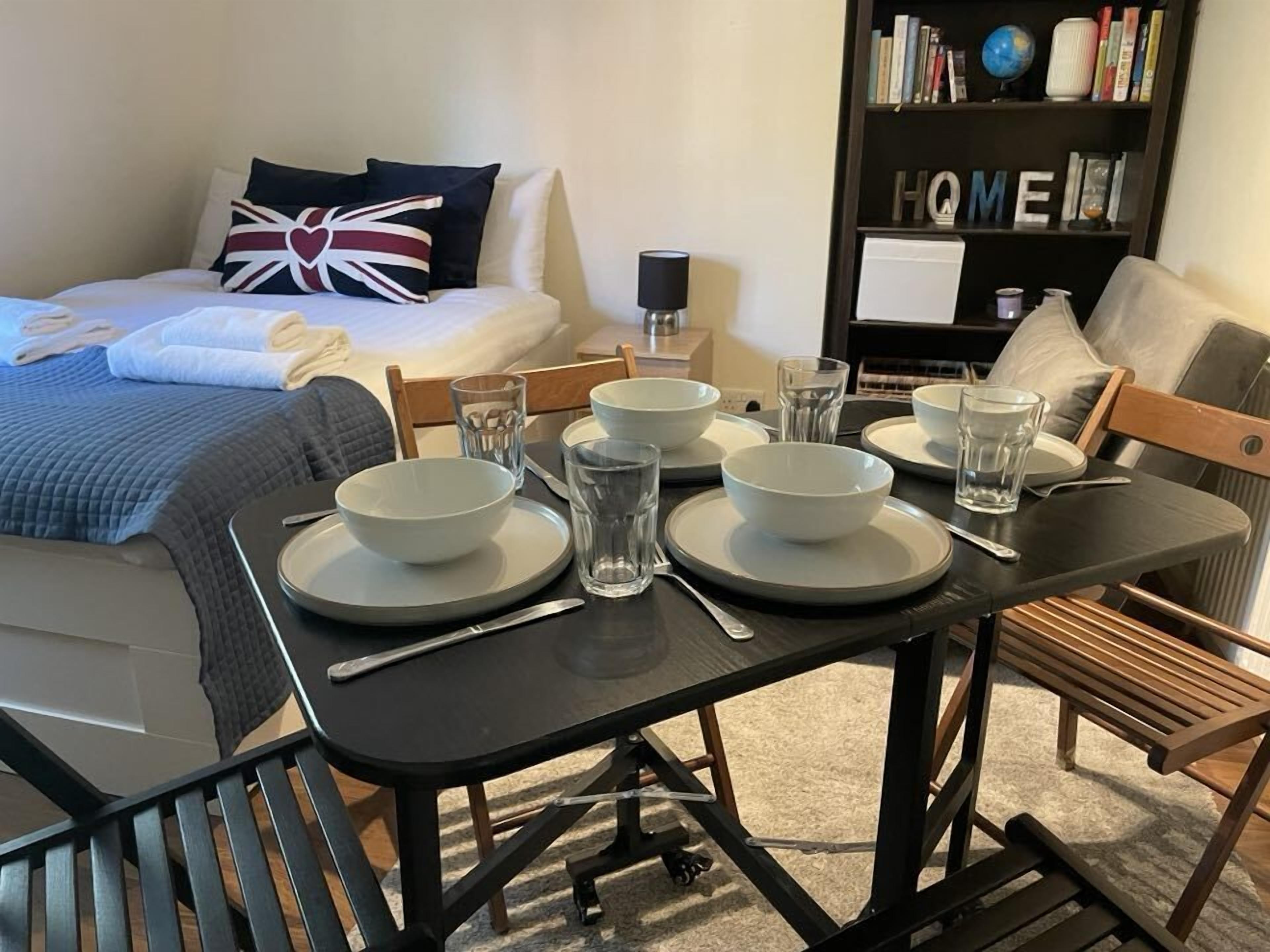 Un comedor ordenado con una mesa lista para cuatro, incluyendo platos, vasos y cubiertos.