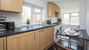 A modern kitchen with wooden cabinets, a built-in oven, a washing machine, and a dining area with a table and chairs.