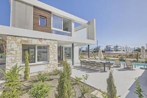 A modern two-story house with a stone facade, a balcony, and a pool area with outdoor furniture. - Villa Kelsi, Stunning and New 5BDR Ayia Napa Villa with Private Pool (Ayia Napa)