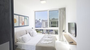 Ett modernt hotellrum med en stor säng, ett nattduksbord, en TV och ett fönster med utsikt över byggnader.