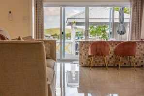 Un salon moderne comprenant un canapé, deux fauteuils, une porte vitrée donnant sur un balcon et un sol carrelé.