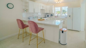 Una cocina moderna con armarios blancos, una isla central con dos sillas rosas, un microondas y un cubo de basura.