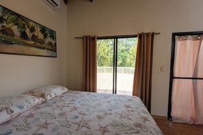 A bedroom with a bed, a painting on the wall, and a view through the window. - Villa with a private pool in Tela! Azalea House (Tela)