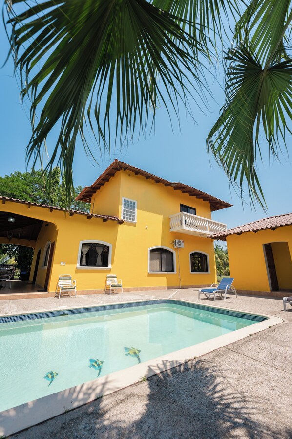 A yellow building with a swimming pool, two balconies, and a covered patio area.