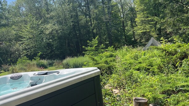 A hot tub in a forested area with a wooden bench and a stone stump nearby. - StarryPinesCottage w Cedar Sauna Steps to Trails (Catskill)