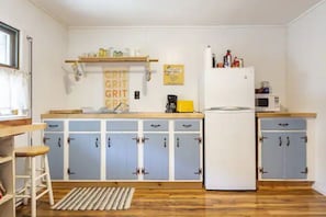 A compact kitchen with blue cabinets, a white refrigerator, and a wooden countertop.