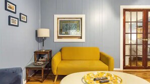 A living room with a yellow sofa, a small table with a lamp, and a framed artwork on the wall. - StarryPinesCottage w Cedar Sauna Steps to Trails (Catskill)