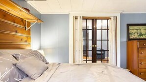 A bedroom with a bed, wooden headboard, a dresser, and a door leading to another room. - StarryPinesCottage w Cedar Sauna Steps to Trails (Catskill)