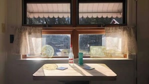 A room with a window overlooking a snowy landscape, a table with a bottle, a glass, and a plate. - StarryPinesCottage w Cedar Sauna Steps to Trails (Catskill)