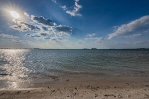 Een strand met heldere lucht en zonlicht dat op het water weerkaatst.