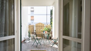 Uma porta aberta que dá para um pátio com mesa, cadeiras e plantas em vasos.