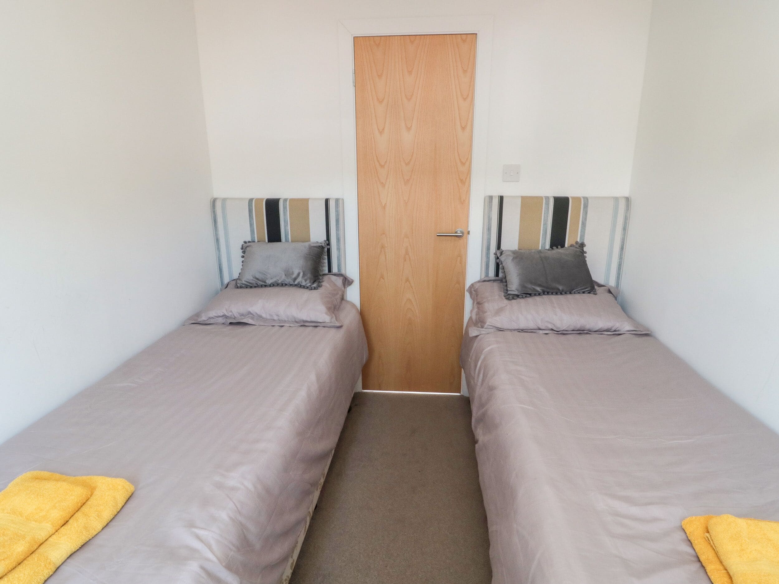 A twin room with two single beds, a wooden door, and a striped headboard.