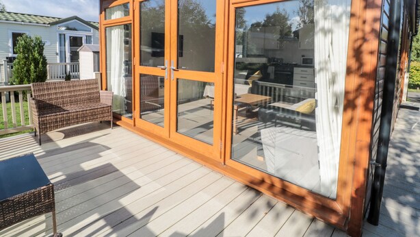 A wooden deck with a glass door leading to a patio area. - Pinecone Lodge - No 9 (Morpeth)
