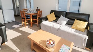 A compact living space with a sofa, a dining table, and a small kitchen area. - Pinecone Lodge - No 9 (Morpeth)