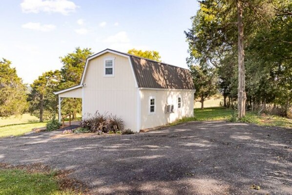 A single-story white building with a sloped roof, a covered porch, and a gravel driveway. - On farm cottage with mountain views. (Bridgewater)