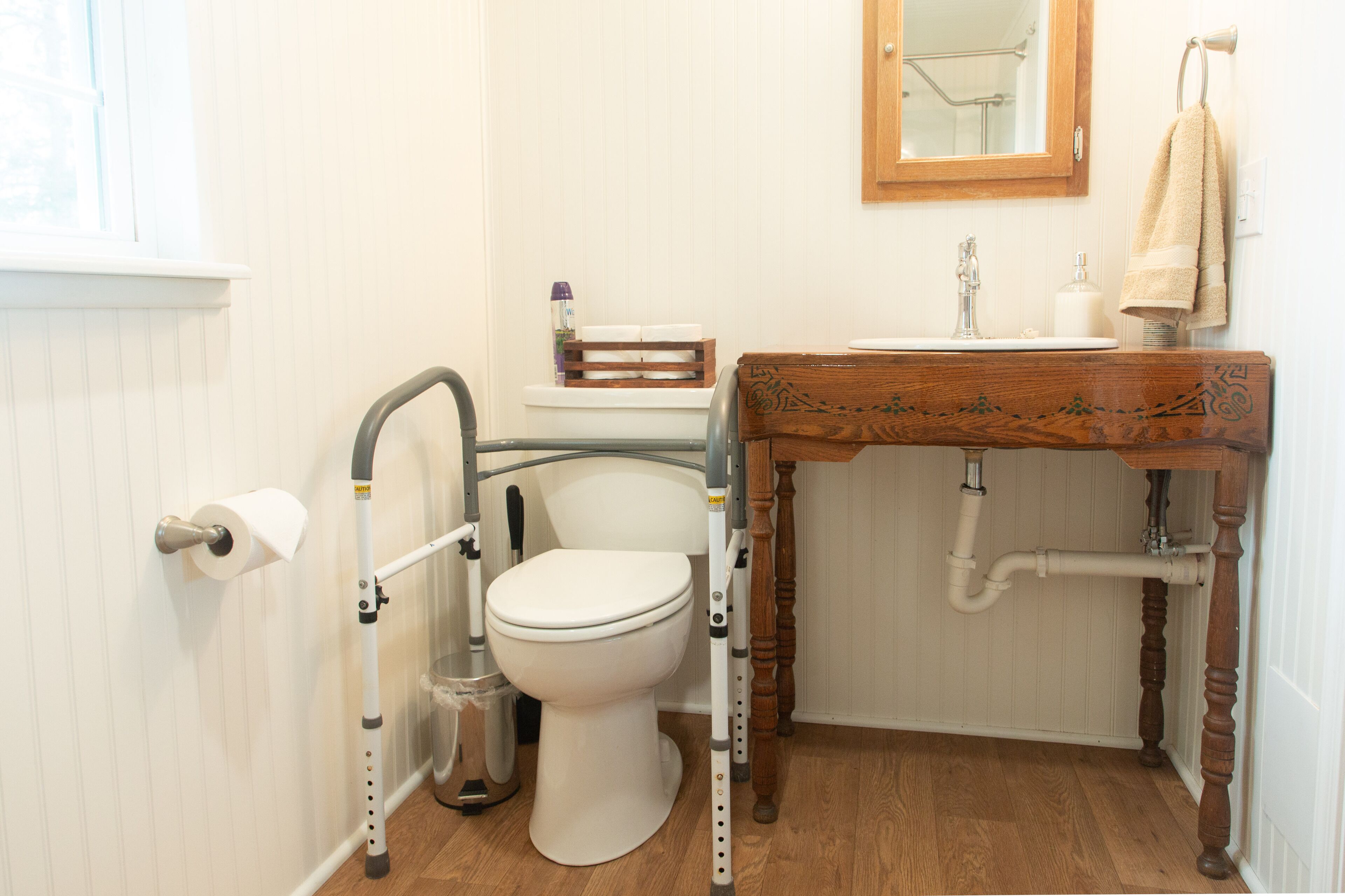 A bathroom with a toilet, a sink with a wooden countertop, a mirror above the sink, and a towel hanging on the wall.