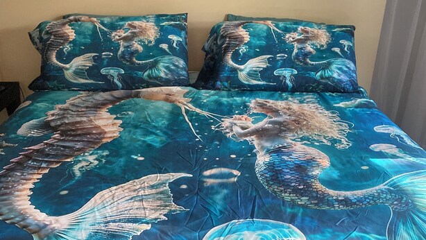 Una cama con edredón y almohadas con motivos de sirena.