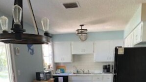 Una cocina con armarios blancos, un refrigerador negro y una mesa de comedor con sillas.