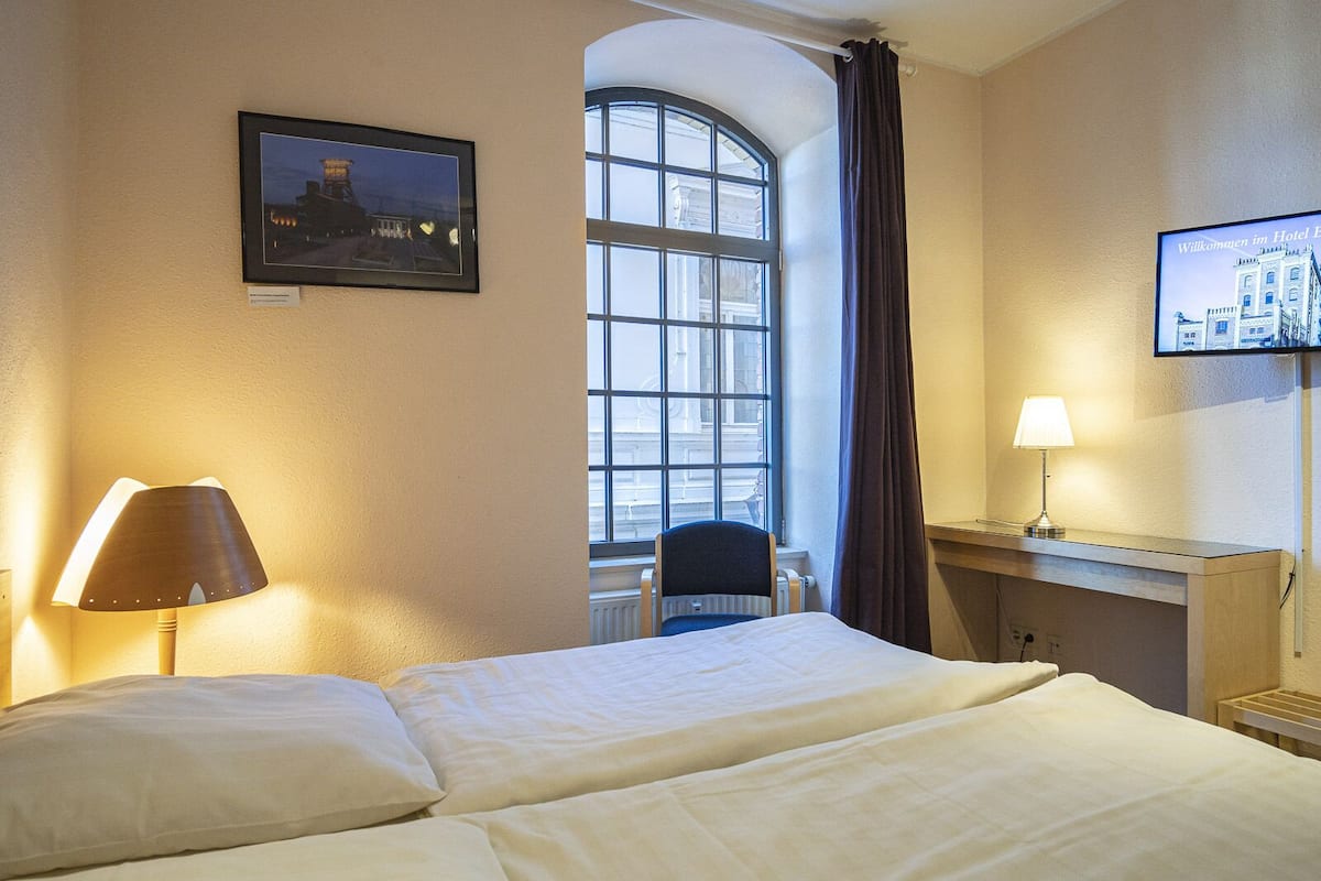 A hotel room with a bed, a desk, a chair, a TV, and a window with curtains.