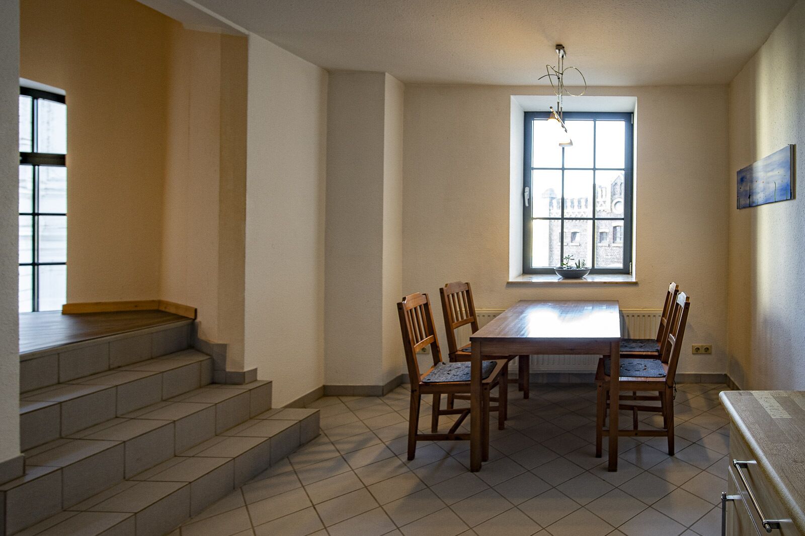 Ein Essbereich mit einem Holztisch und Stühlen, einem Fenster mit Blick auf Gebäude und einer Treppe, die in eine obere Ebene führt.