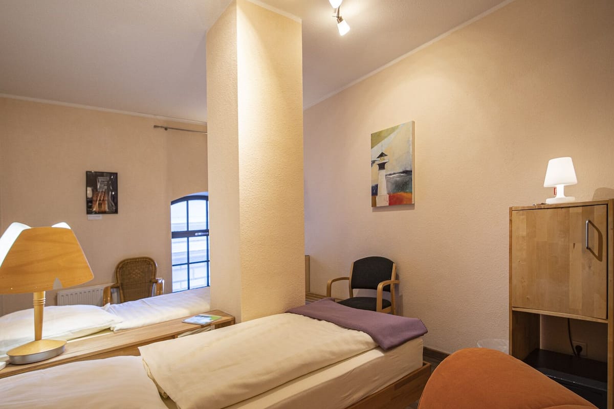 A hotel room with two beds, a chair, a cabinet, and a painting on the wall.