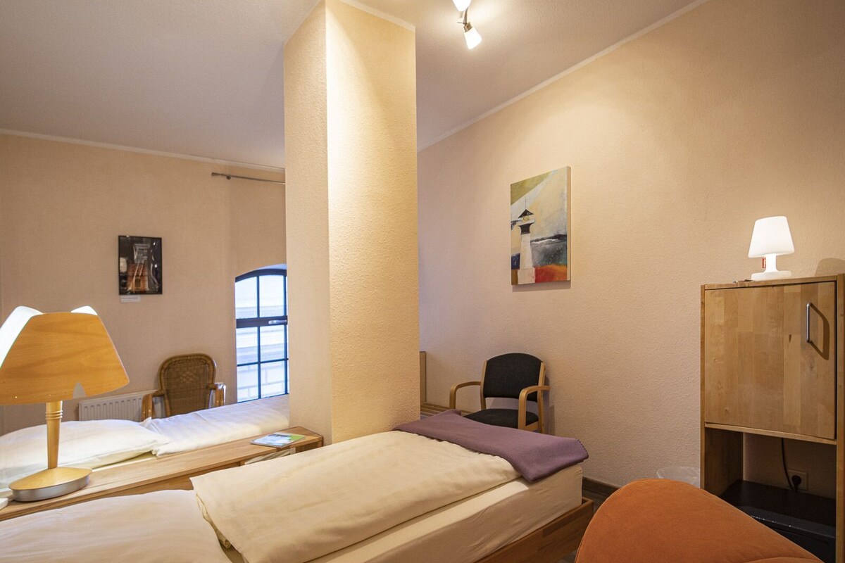Una habitación de hotel con dos camas, una silla, un armario, una lámpara y un cuadro en la pared.