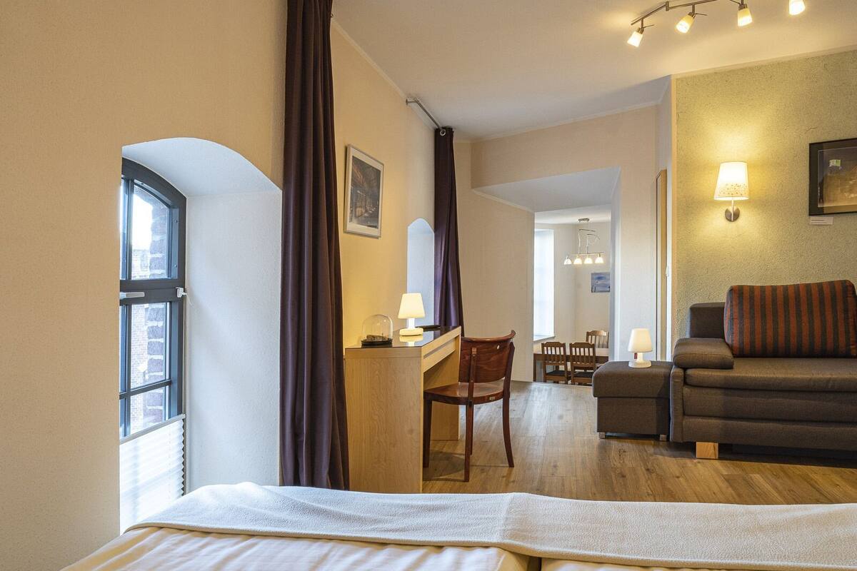 A hotel room with a bed, a desk, a chair, a sofa, and a dining area.