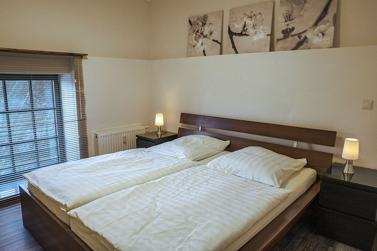 A double bed with two bedside tables, a radiator, and a window with blinds.