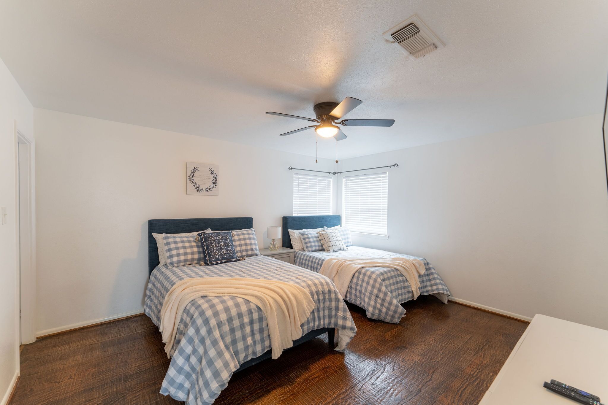 A bedroom with two beds, a ceiling fan, and a window with blinds.