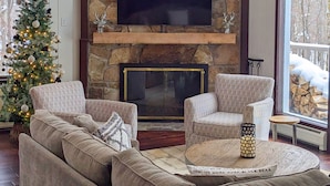 Una sala de estar acogedora con chimenea de piedra, un televisor de pantalla plana grande y un árbol de Navidad.